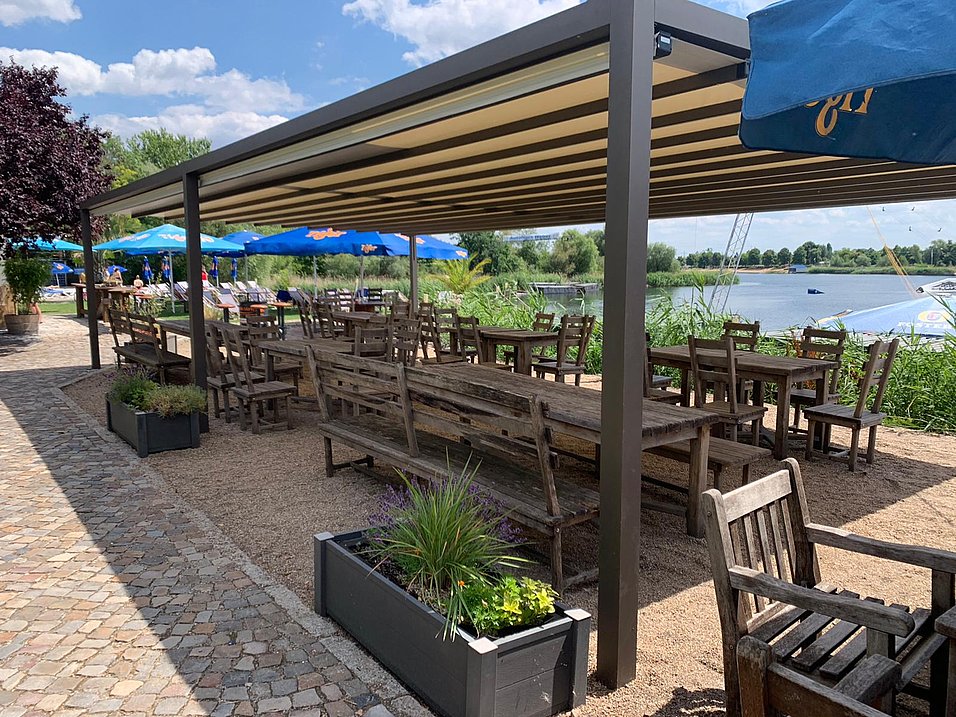Überdachte Seeterrasse einer Gastronomie mit Pergola-Markise und Wasserblick
